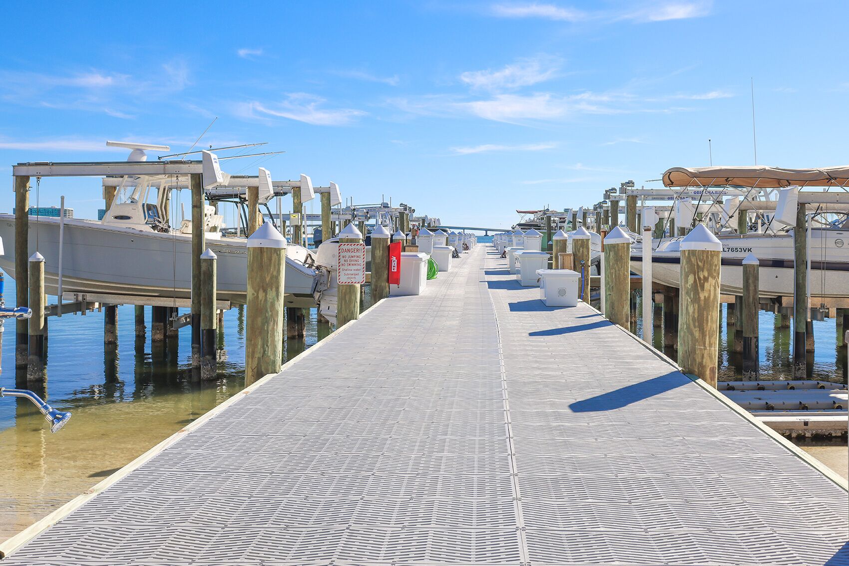 A pier with boats docked on both sides, a clear sky, and a sign warning against jumping into the water.