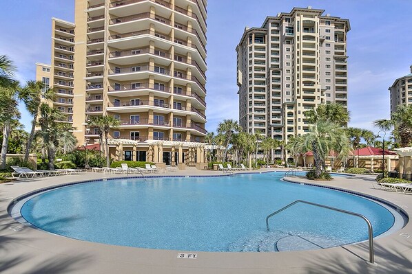 A swimming pool with a 3 FT depth marker, surrounded by palm trees and modern high-rise buildings.