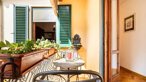 Un étroit couloir extérieur avec une chaise en métal, une petite table sur laquelle est posée une bougie, et des plantes en pot.