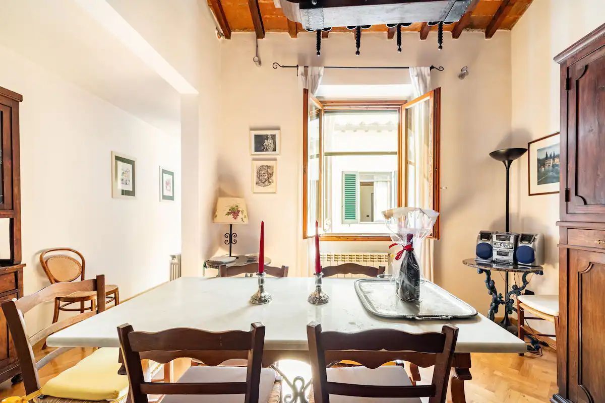 Uma sala de jantar com uma mesa comprida, cadeiras de madeira e um rádio sobre uma mesinha.