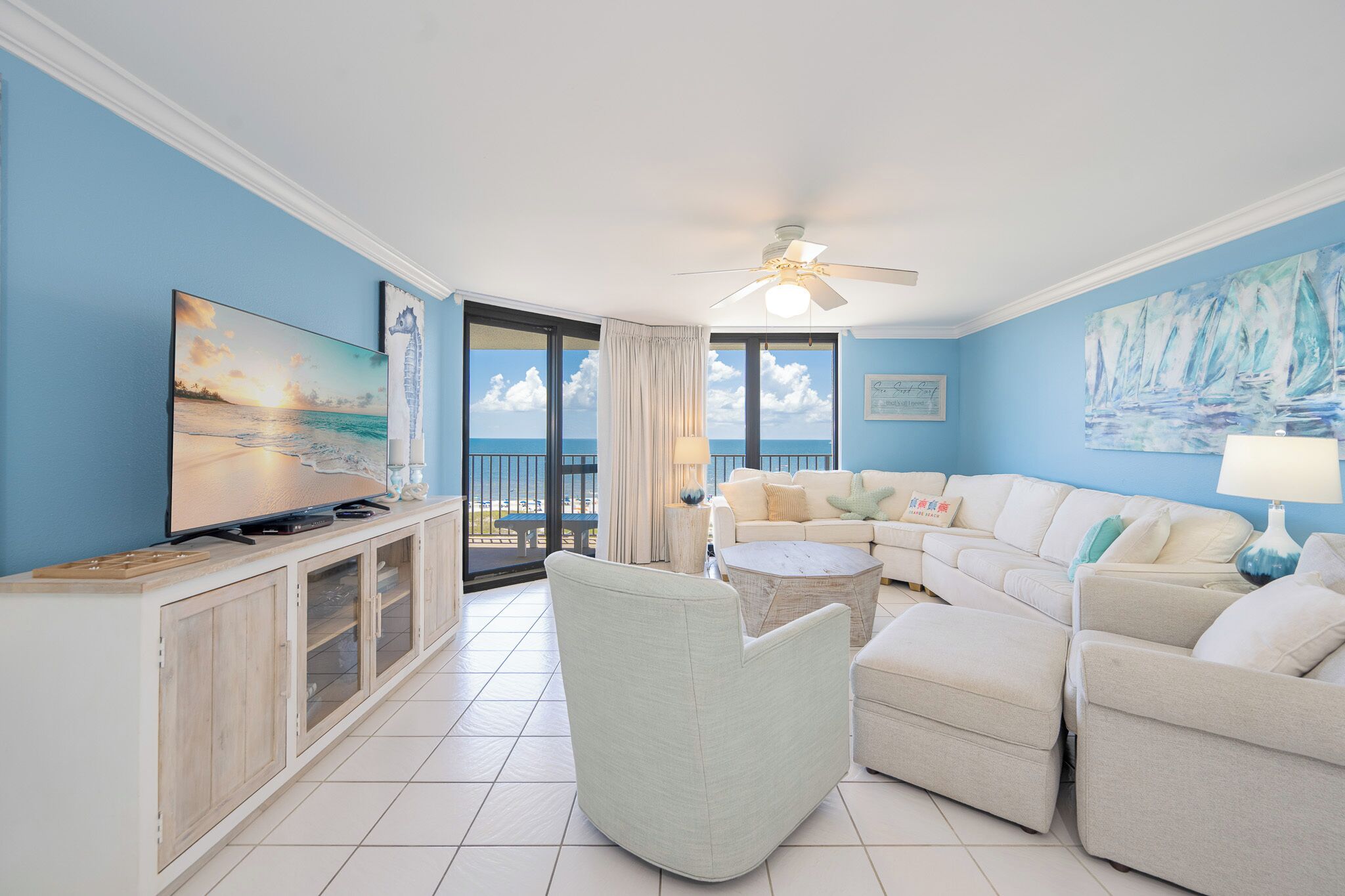 A living room with a television, a sofa, a coffee table, and a view of the ocean through large windows.