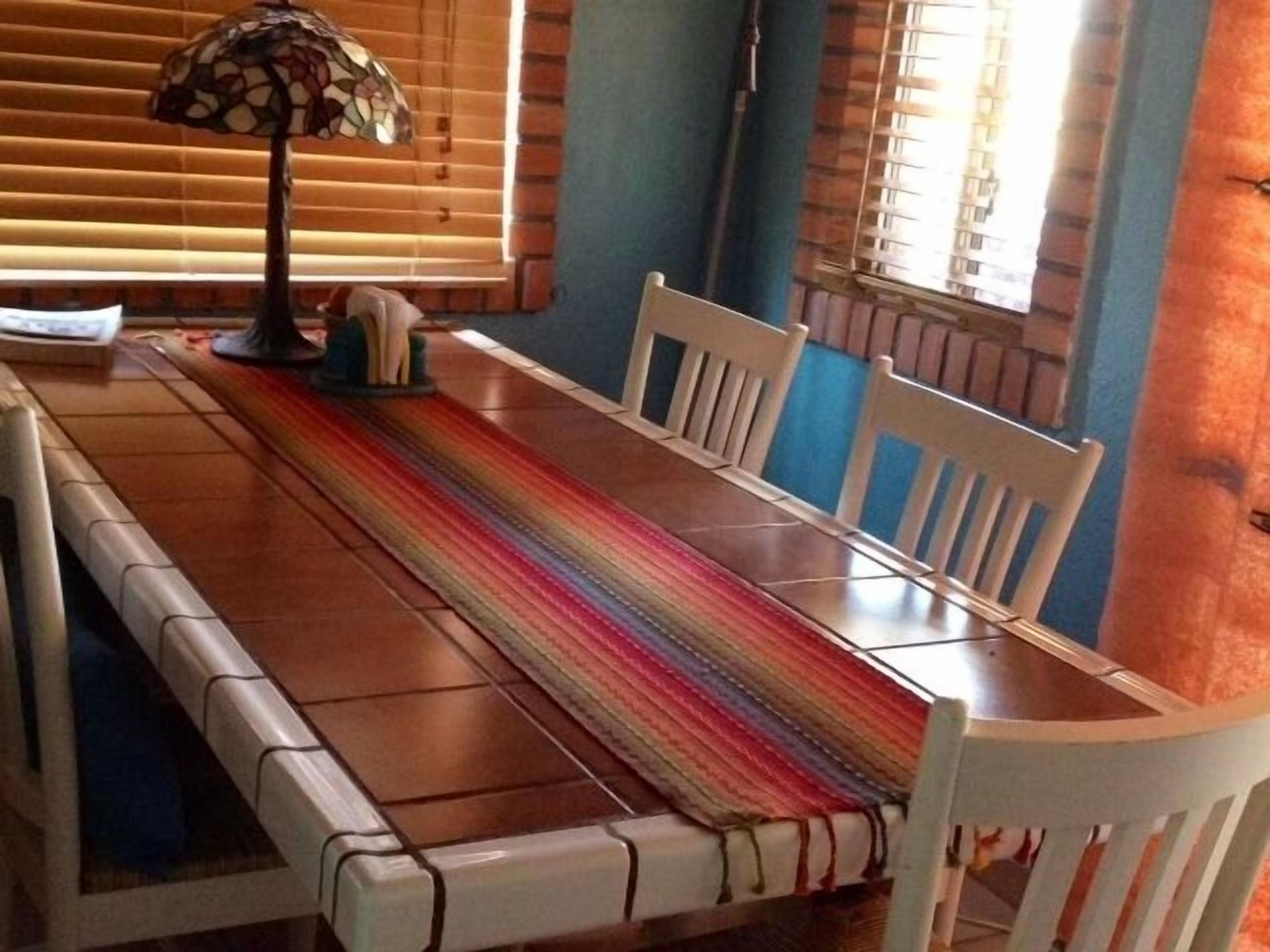 Un tavolo da pranzo con sedie, un runner a righe e una lampada.