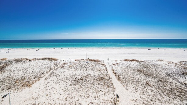 Une vaste plage de sable fin, sous un ciel bleu dégagé et une mer calme.