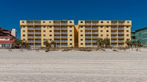 Un hôtel à plusieurs étages doté de balcons, situé sur une plage de sable fin bordée de palmiers.
