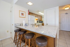 Una cocina con encimera de mármol, taburetes de madera, un refrigerador, un microondas y un reloj en la pared.