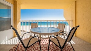 Une table ronde entourée de quatre chaises, sur un balcon donnant sur la plage.