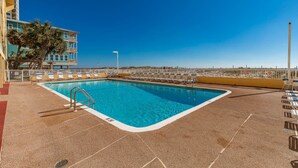 Une piscine à l’eau d’un bleu cristallin, entourée de chaises longues et bordée d’un bâtiment doté de balcons.