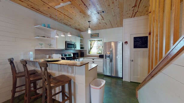 A kitchen with wooden cabinets, a stainless steel refrigerator, a microwave, and a window with curtains. - Pet Friendly, Located in Town, Close to beach, Shared Pool, Golf Cart Access (Port Aransas)