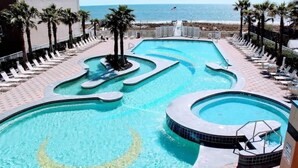 A pool area with multiple swimming sections, palm trees, and a view of the beach. - Crystal Tower 1509 - Luxurious 15th Floor Corner Condo with Breathtaking Views (Gulf Shores)