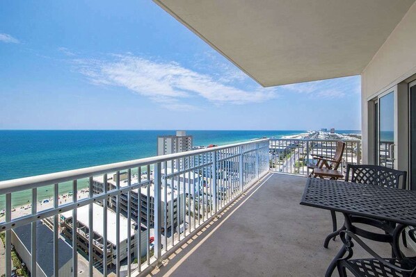 Un balcon avec vue sur l’océan et la plage, une table et des chaises.