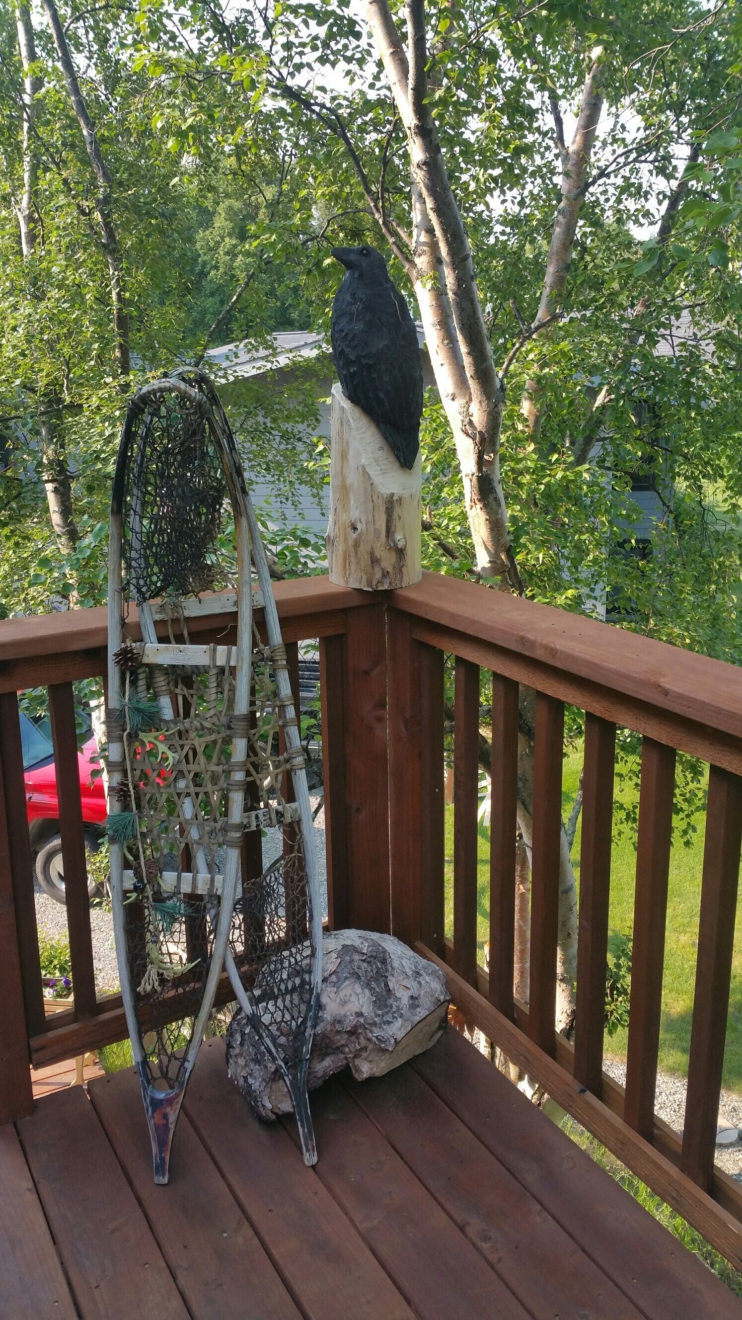 Een houten terras met een vogelhuisje en een vogel op een paal.