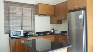 A compact kitchen with wooden cabinets, a stainless steel refrigerator, a microwave, and a gas stove. - Villa Somewhere Phuket Laguna Bangtao (Choeng Thale)