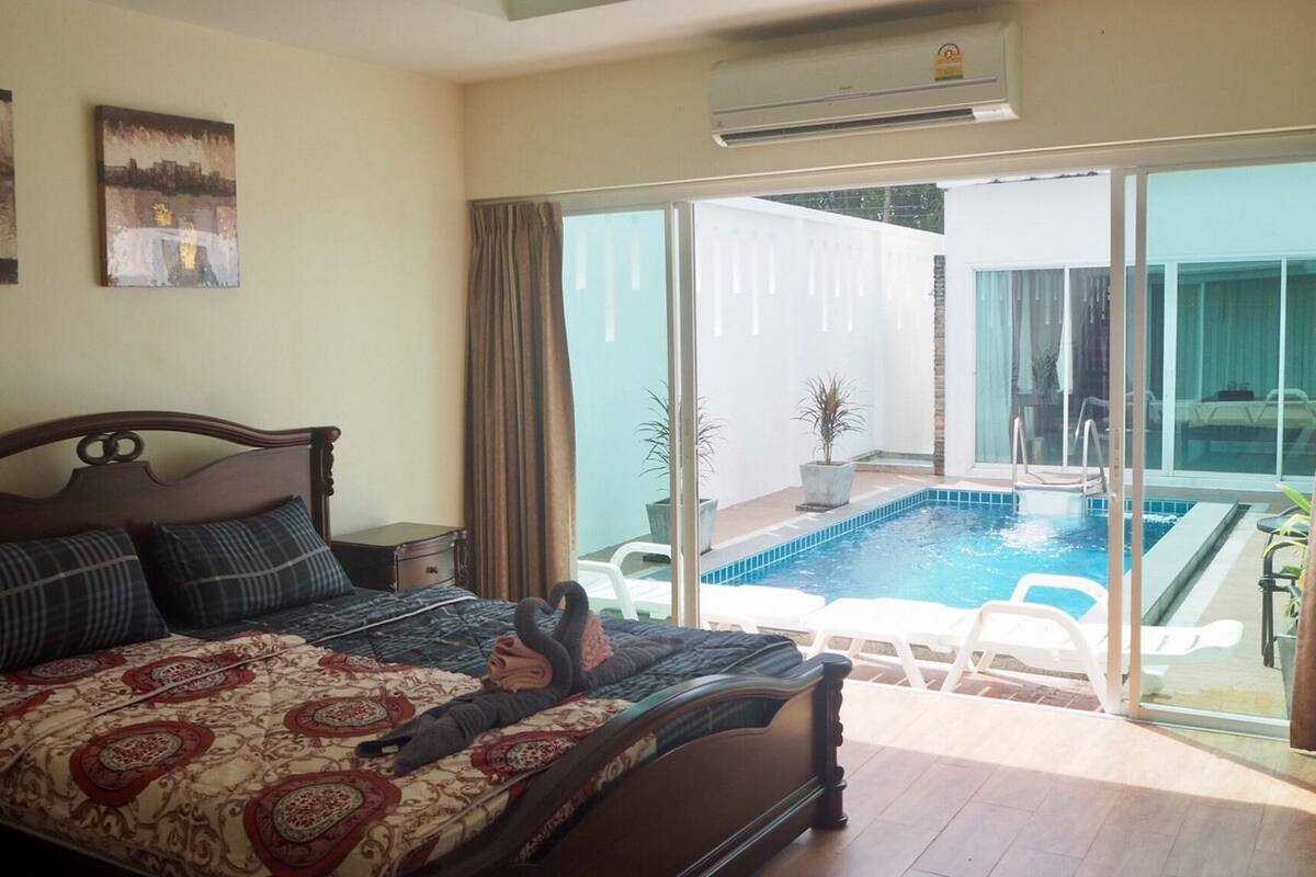 A bedroom with a large bed, a view of a swimming pool, and two paintings on the wall.