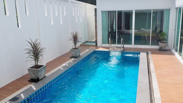 A rectangular indoor swimming pool with clear blue water, surrounded by a tiled deck and potted plants. - Villa Somewhere Phuket Laguna Bangtao (Choeng Thale)