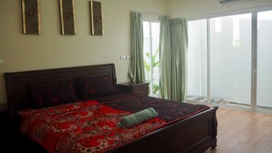 A bedroom with a large bed, a nightstand, a window with curtains, and a view of the outside. - Villa Somewhere Phuket Laguna Bangtao (Choeng Thale)