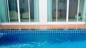 A swimming pool with a tiled edge, a wooden deck, and a view of a room with a bed and curtains. - Villa Somewhere Phuket Laguna Bangtao (Choeng Thale)