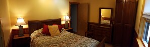 A bedroom with a bed, two bedside lamps, a dresser, a mirror, and a door. - Log Cabin with Hot Tub, Sauna, Private Pond, 23 acres -- 4.6 mi to Bethel Woods (Cochecton)
