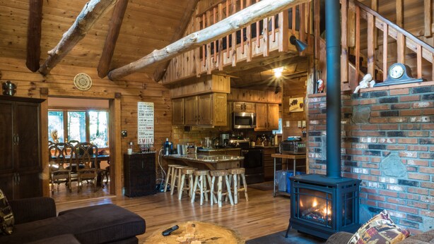 Un intérieur de chalet chaleureux avec un coin repas en bois, une cuisine équipée d’appareils modernes et une cheminée.
