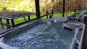 Un bain à remous sur une terrasse en bois, avec vue sur une zone herbeuse et des arbres.
