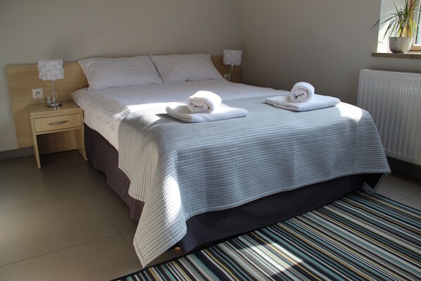 A neatly made bed with a striped bedspread, two white towels, a bedside table with a lamp, and a potted plant on a windowsill. - Eco Nieborów (Nieborów)