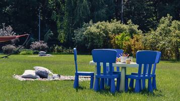 En picknickplats med ett bord och stolar på en gräsyta, omgiven av träd och buskar.