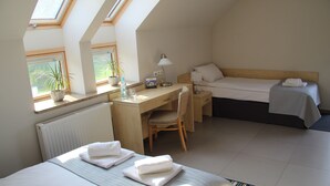 Habitación de hotel con cama, escritorio, silla, mesita, lámpara y ventana con planta.