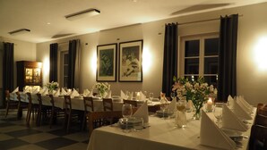 Un comedor con mesas dispuestas para una comida, obras de arte en las paredes y un ventanal con cortinas.