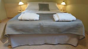 Un lit bien fait, avec deux serviettes pliées posées sur le dessus, deux lampes de chevet et un oreiller sur la tête de lit.