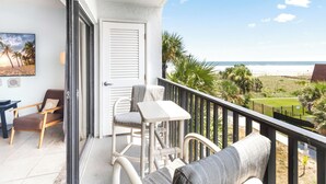 Ein Balkon mit Blick auf den Strand, mit einem Stuhl, einem Tisch und einer Couch.
