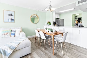 A modern kitchen with white cabinets, a wooden dining table, and a hanging light fixture.