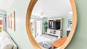 A room with a large mirror reflecting a dining area, a television, and a ceiling fan. - Perfect Family Getaway Steps from Cocoa Beach Pier with Oceanfront Heated Pool (Cocoa Beach)