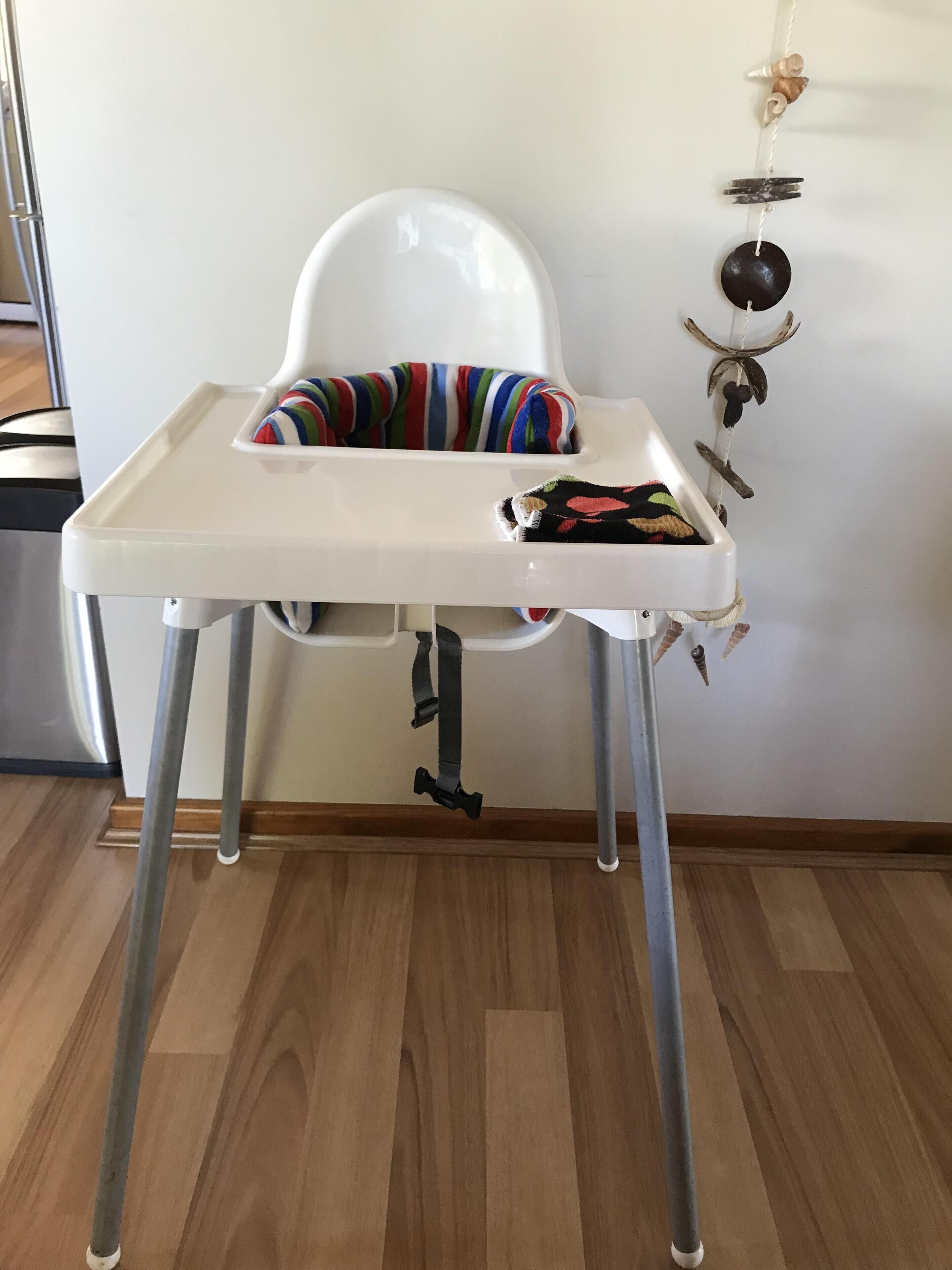 A white high chair with a tray, positioned against a white wall.