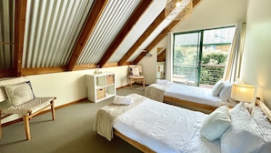 A bedroom with two beds, a wooden chair, a small table, and a large window with a view of greenery. - 5 bedroom 2 bathroom family beach house with glimpses of Geographe Bay (Dunsborough)