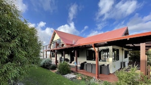 A two-story house with a red roof, a covered porch, and a garden with various plants and flowers. - 5 bedroom 2 bathroom family beach house with glimpses of Geographe Bay (Dunsborough)