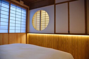 Una habitación tradicional japonesa con suelo de tatami, una cama de madera baja y puertas correderas shoji.