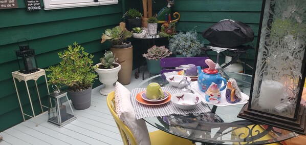 A glass table set with plates, cups, and decorative items on a balcony with potted plants and a green wall. - Cat On The  Hat Cottage ~MeOw MeOw~
5 stars 🌟🌟🌟 🌟 🌟 😻 property
PURRRFECT

 (Blackheath)