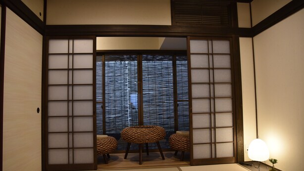 Una habitación japonesa tradicional con suelo de tatami, puerta corredera shoji y una pequeña mesa con cojines.