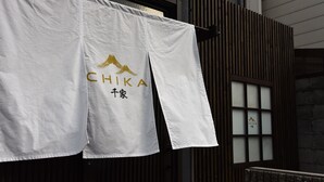 Un lienzo blanco con el logotipo y el nombre "CHIKA" colgado de un edificio.