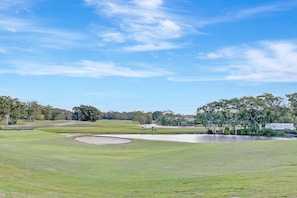 A golf course with a sand bunker, a water hazard, and a sign reading 'HORIZONS'.