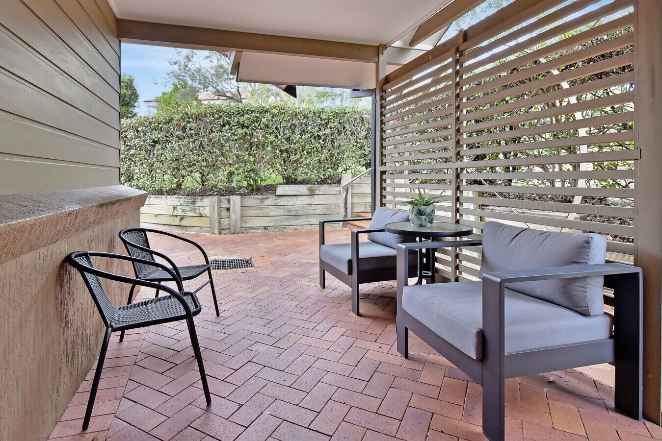 A patio with a brick floor, a table, two chairs, and a wooden fence.
