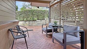 A patio with a brick floor, a table, two chairs, and a wooden fence.