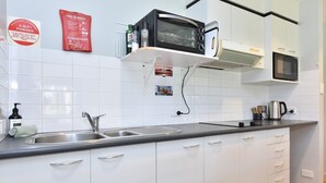 Ett modernt kök med vita skåp, en svart bänkskiva, en mikrovågsugn, en liten ugn med grillfunktion och en vattenkokare.