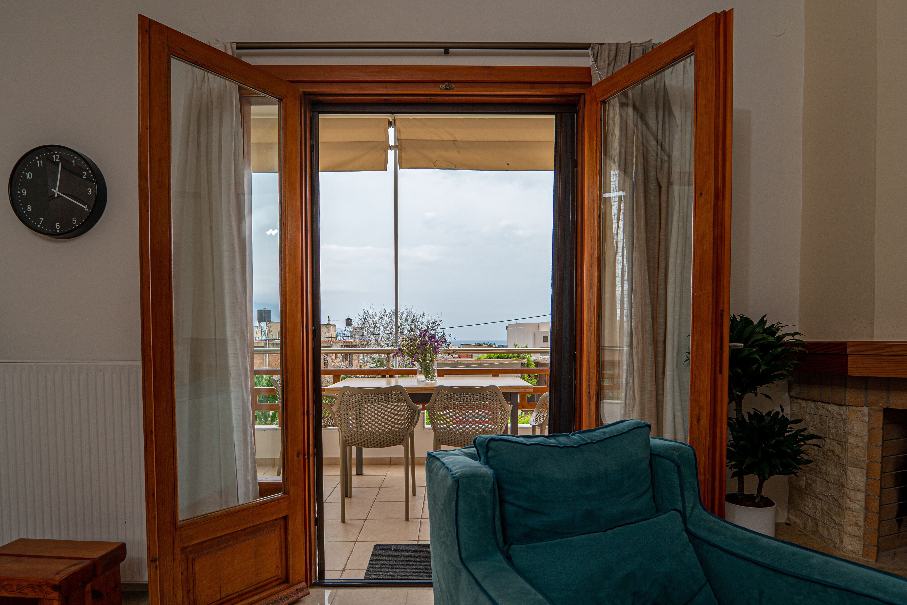 Un salon avec un canapé de couleur turquoise, une porte en bois donnant sur un patio extérieur, une horloge au mur et une plante en pot.