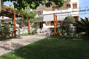 Een binnenplaats met een pergola, plantenpotten en een pad dat naar een gebouw met balkons leidt.