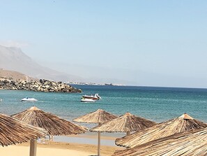 A beach with thatched umbrellas, a rocky shoreline, and boats in the water. - Contemporary 2 bedroom apt, close to the best beaches of Crete!  (Kissamos)