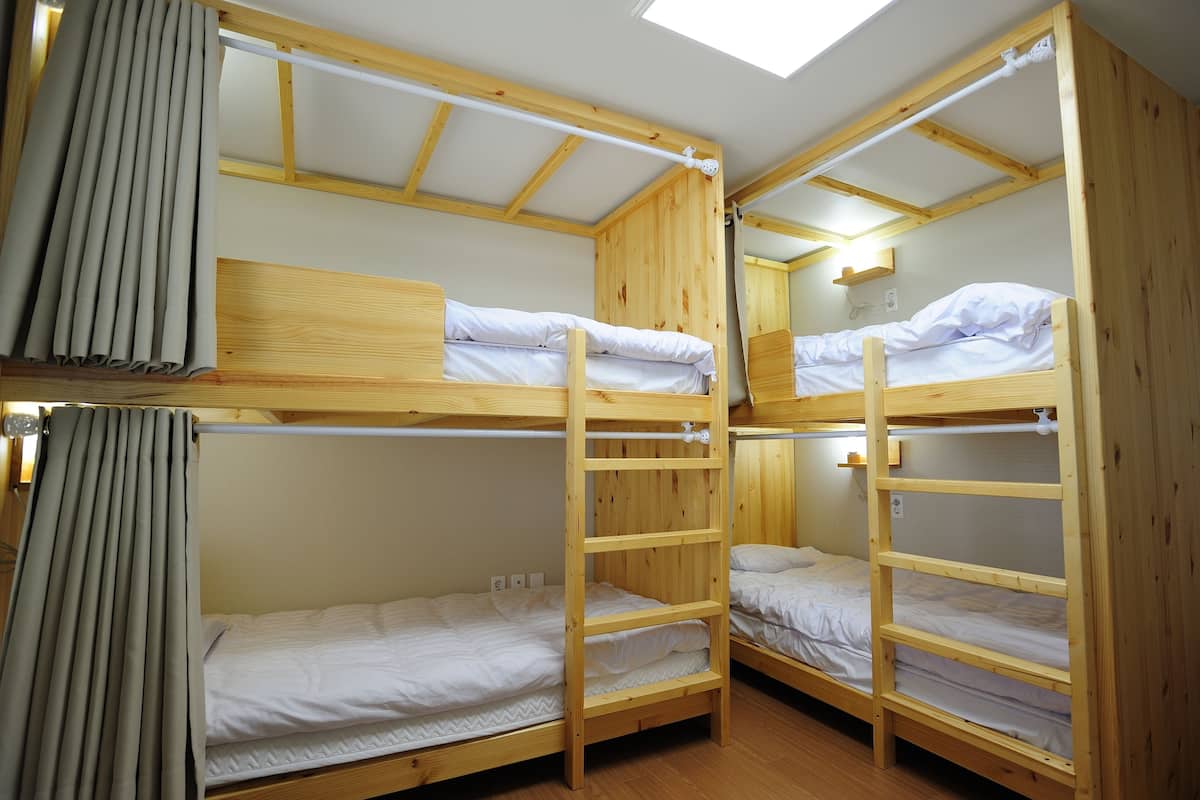 Dormitorio con literas de madera, tragaluz y cortina.