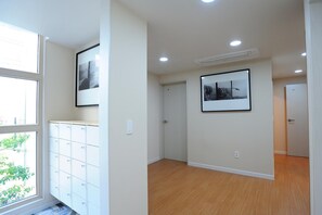 A spacious room with wooden flooring, a white cabinet with multiple compartments, and two framed pictures on the walls. - Hannah Guest House - Hostel (Jeju City)