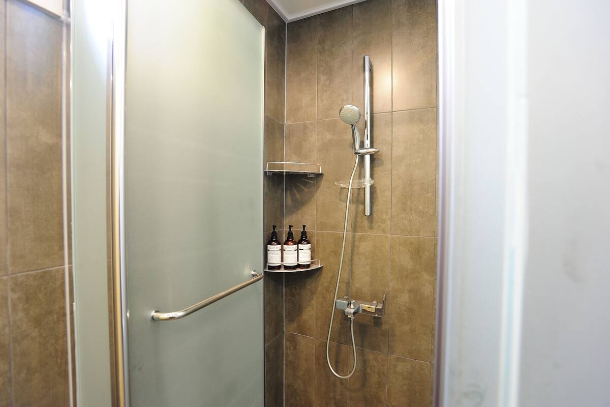 Ducha con cabezal de ducha de mano, grifo empotrado en la pared y estante con artículos de aseo.
