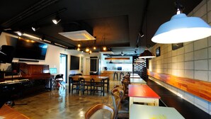 A restaurant with a long counter, multiple tables, and chairs. There is a piano and a television on the left side.