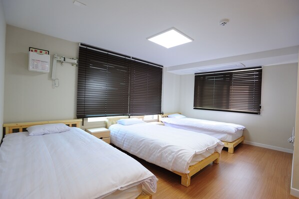 A room with three single beds, wooden flooring, and large windows with blinds. - Hannah Guest House - Hostel (Jeju City)